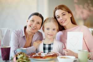 Girl, her mother and grandmother sitting by table and looking at camera